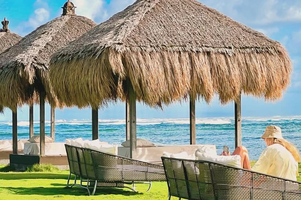 Guests relaxing under thatched beach shelters beside the ocean